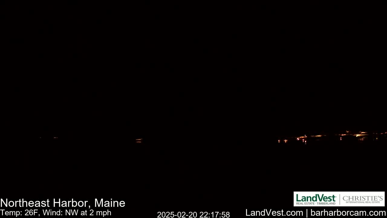 A nighttime long shot shows a dark, mostly black sky with a faint line of distant lights on the horizon under a northwest wind of 2 mph at 26°F.