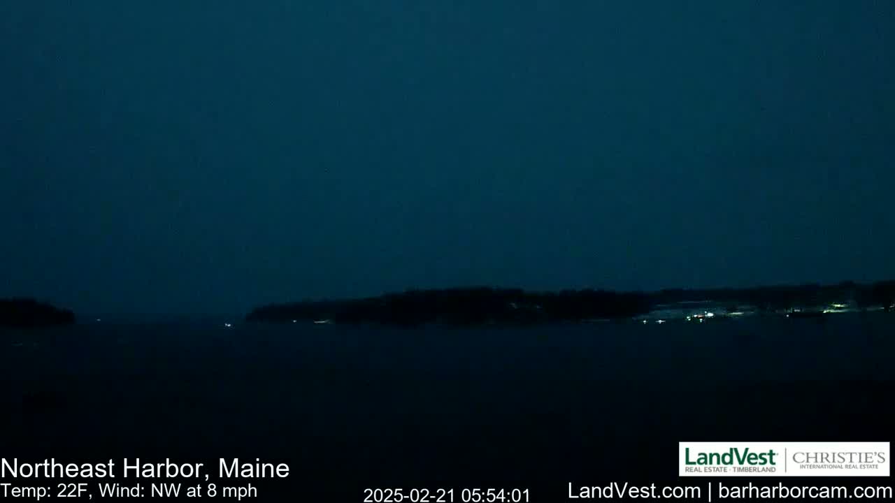 A dark, nighttime view of a calm body of water with a shoreline in the distance under a clear, dark blue sky.
