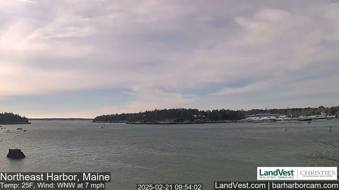 A calm harbor with a snow-dusted shoreline under a partly cloudy sky, a gentle wind blowing from the west-northwest at seven miles per hour and a temperature of twenty-five degrees Fahrenheit.