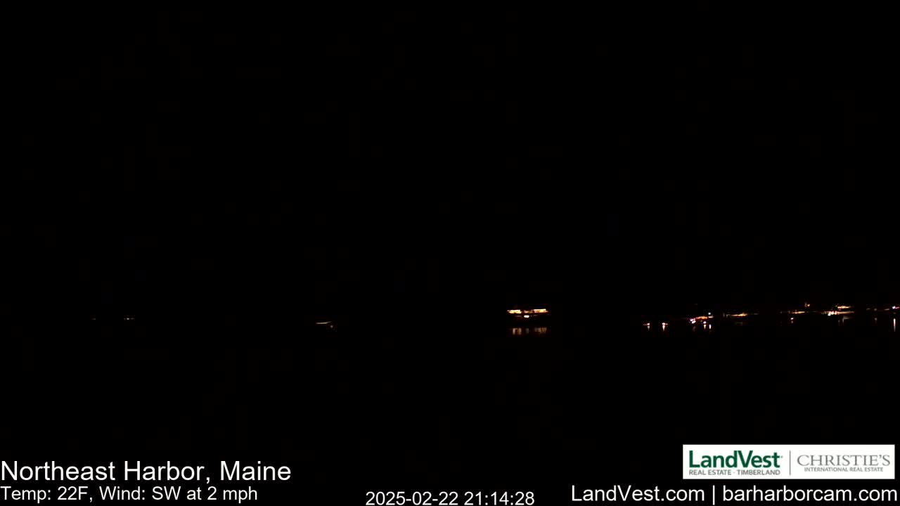 At night, a dark body of water reflects the faint lights of buildings in the distance, under a clear, 22°F sky with a southwest wind of 2 mph.