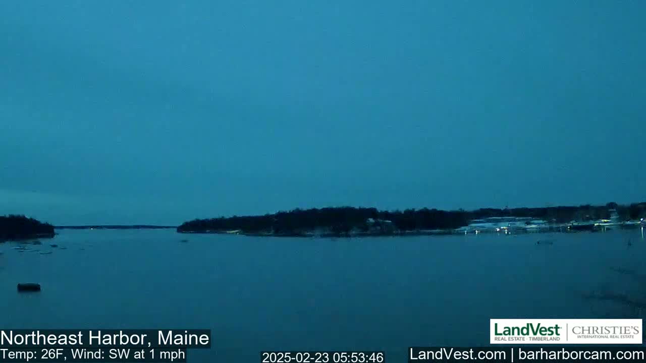 A calm, dark-blue body of water is seen at twilight, with a low shoreline of dark trees visible in the distance.