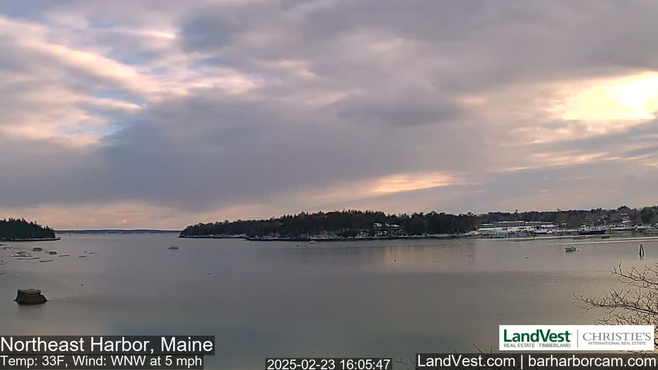 A calm harbor with snow-dusted shorelines under a partly cloudy sky at sunset.