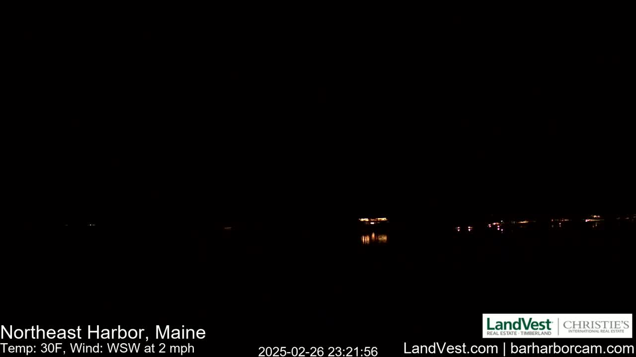 A nighttime view of a dark body of water with a few distant lights reflecting on the surface, under a clear, dark sky with a temperature of 30°F and a WSW wind at 2 mph.