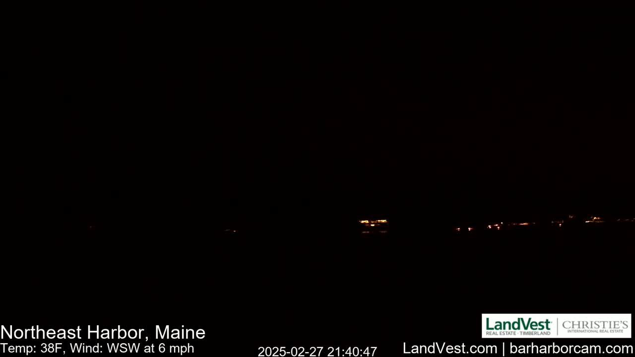 A dark nighttime scene shows a faint line of distant lights across a black horizon under a clear, dark sky.