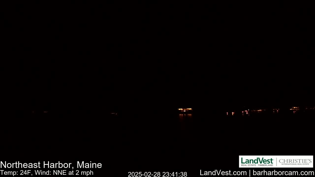 A dark nighttime scene shows a few faint lights across a body of water under a clear, dark sky with a 24°F temperature and a 2 mph northeast wind.