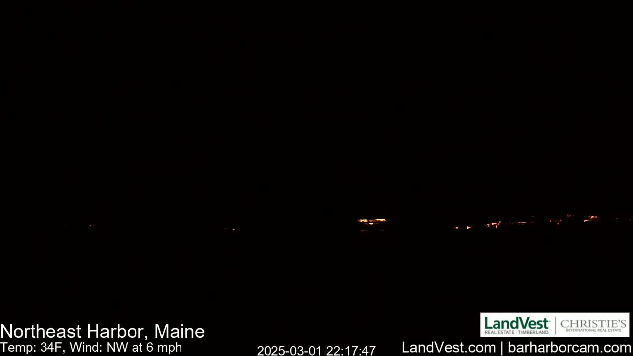 A dark nighttime scene shows a distant line of faint orange lights, with a northwest wind at 6 mph and a temperature of 34°F.
