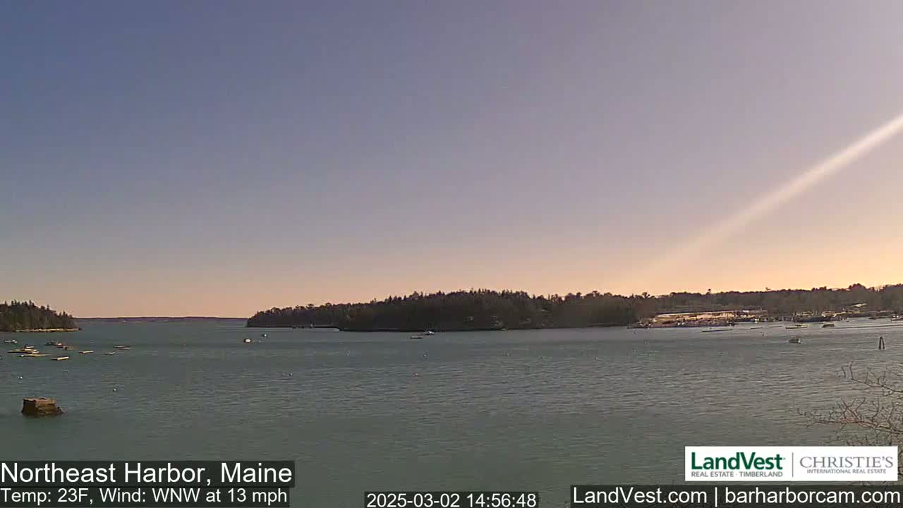 A calm harbor with low-lying land on either side under a clear, pale sky with a slight sunset hue, and a 13 mph wind from the west-northwest at 23 degrees Fahrenheit.
