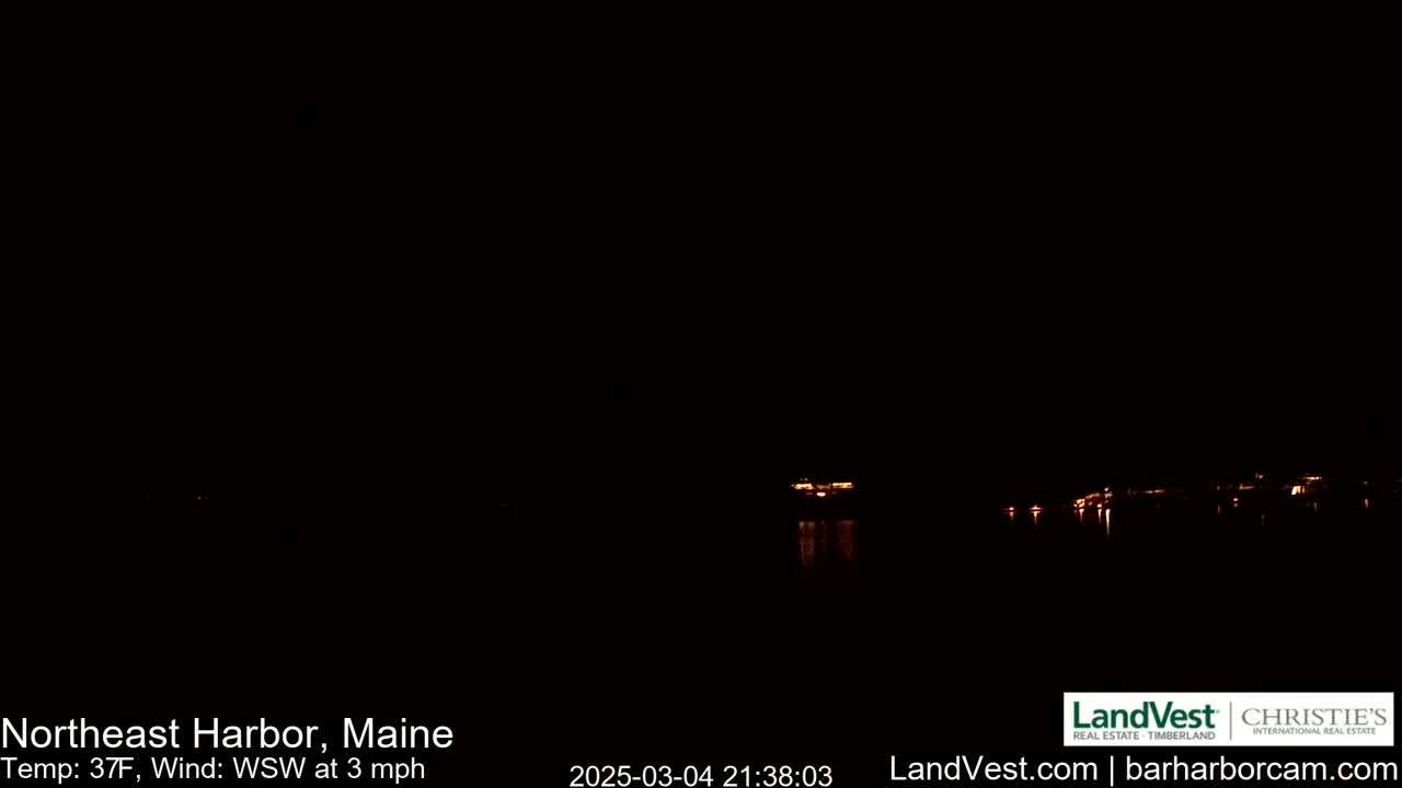 A nighttime view of a calm body of water with faintly visible lights on the opposite shore under a dark sky, with a temperature of 37°F and a west-southwest wind of 3 mph.