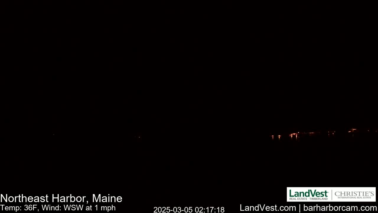 A dark nighttime scene shows a faint line of lights on the horizon across a body of water, with a 36°F temperature and a 1 mph wind from the west-southwest.