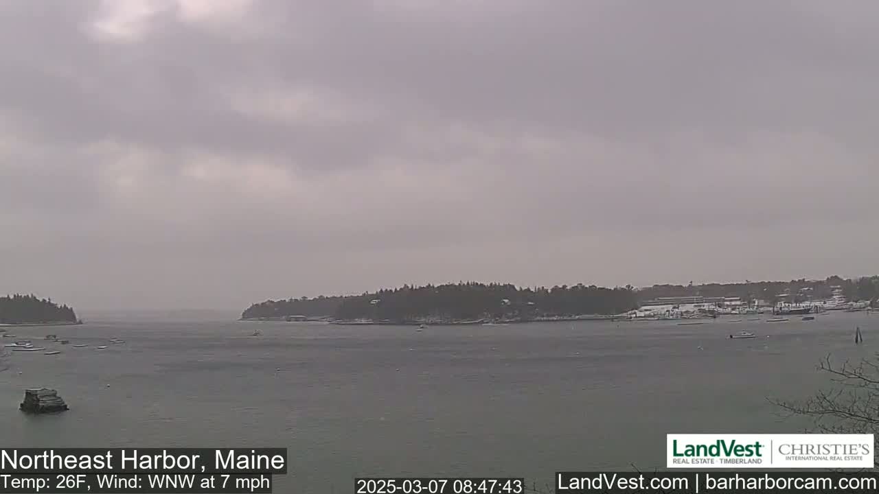 A calm, overcast harbor scene with a few boats and snow-covered land in the distance, under a 26°F temperature and a 7 mph west-northwest wind.