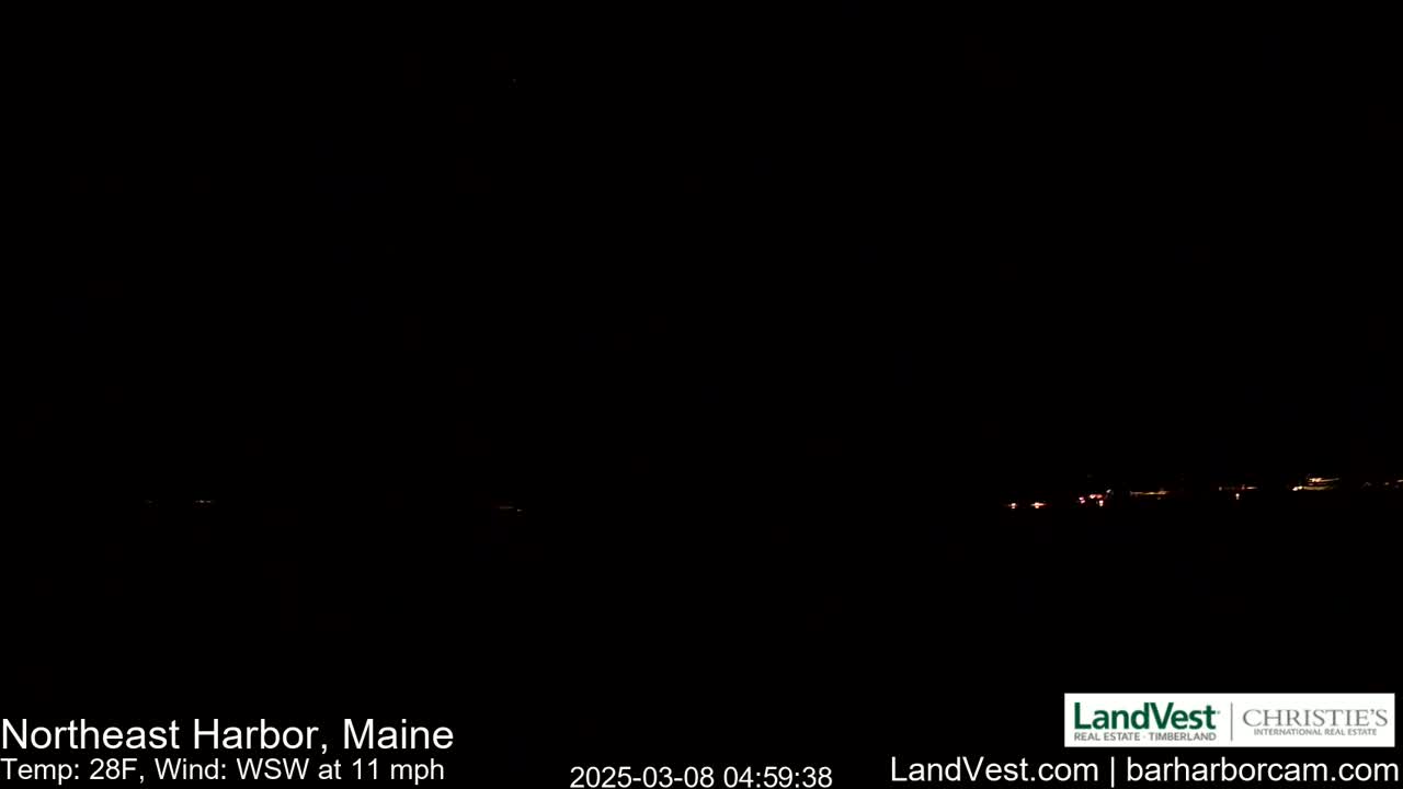 A nighttime, dark scene shows a distant line of faint lights across the horizon under a clear, dark sky, with a 28°F temperature and a 11 mph wind from the west-southwest.