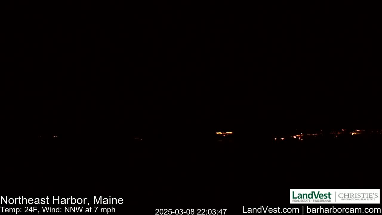 A dark nighttime scene shows a distant line of faint orange lights on the horizon, with a north-northwest wind blowing at 7 mph and a temperature of 24 degrees Fahrenheit.