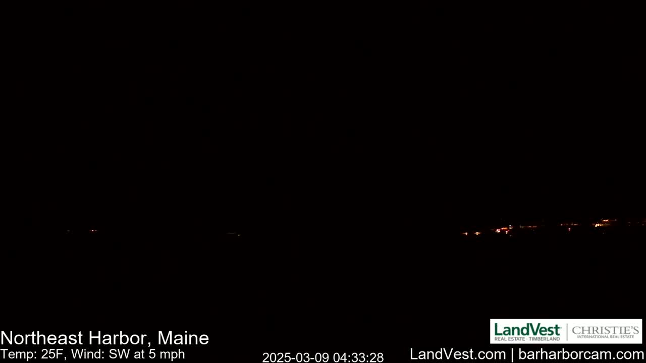 A dark nighttime scene shows a faint, distant glow of lights on the horizon under a clear, dark sky, with a temperature of 25°F and a southwest wind at 5 mph.