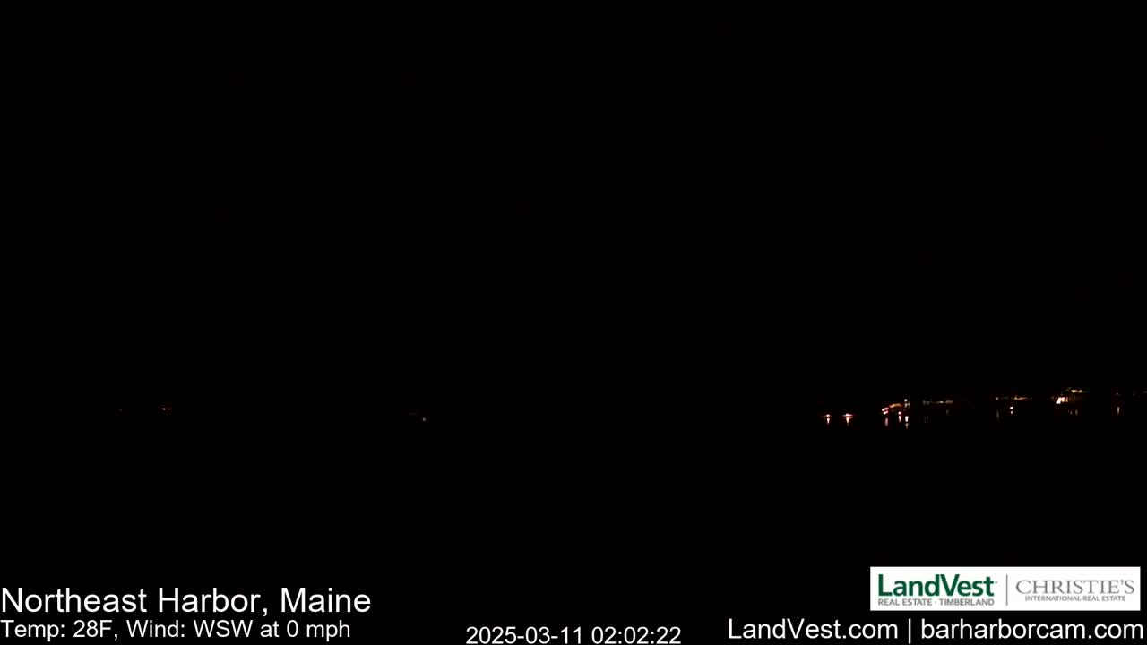 A nighttime, dark image shows a faint line of lights across the bottom of the frame, with a calm, 28-degree temperature and no wind.
