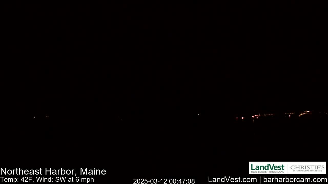 A dark nighttime scene shows a distant line of faint lights across a dark body of water under a clear, dark sky with a southwest wind at 6 mph and a temperature of 42°F.
