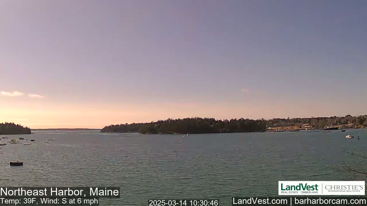 A calm body of water, under a pale, mostly clear sky at sunset, is surrounded by low-lying, wooded land.