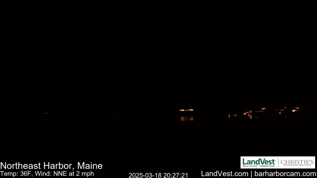 A nighttime view of a dark body of water with faintly visible lights on the opposite shore under a clear, dark sky.