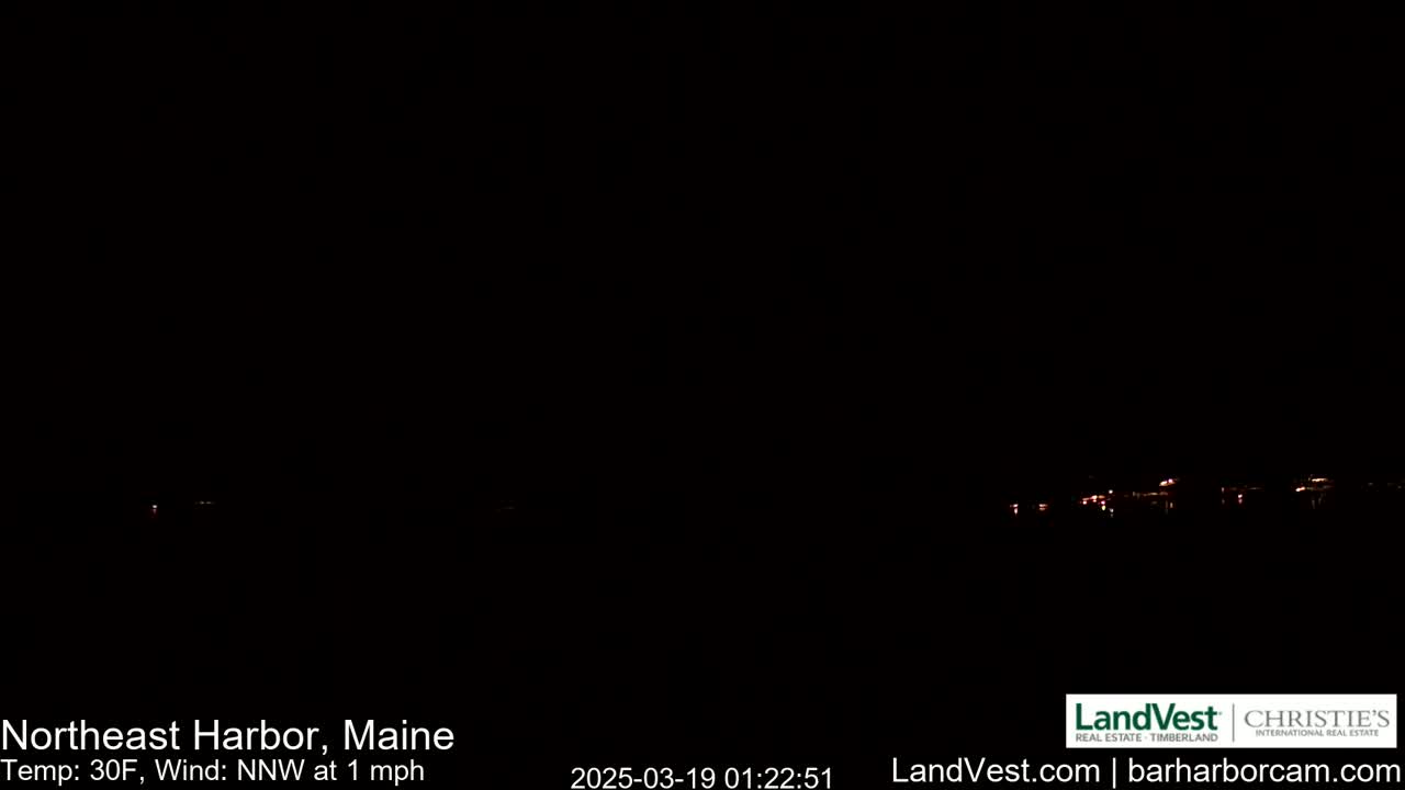 A nighttime, dark image shows a distant, faintly lit shoreline under a clear, dark sky with a 30°F temperature and a 1 mph northwest wind.