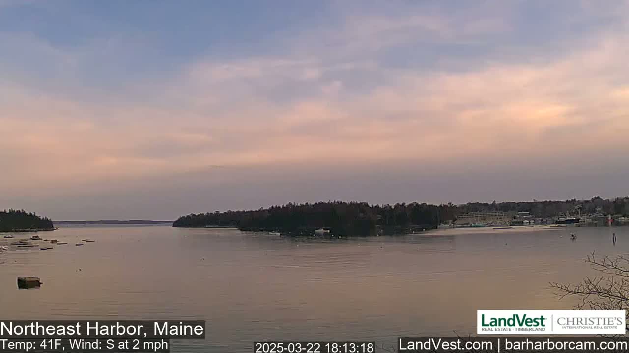 A calm body of water, under a pale pink and blue twilight sky, is surrounded by dark, tree-covered land.
