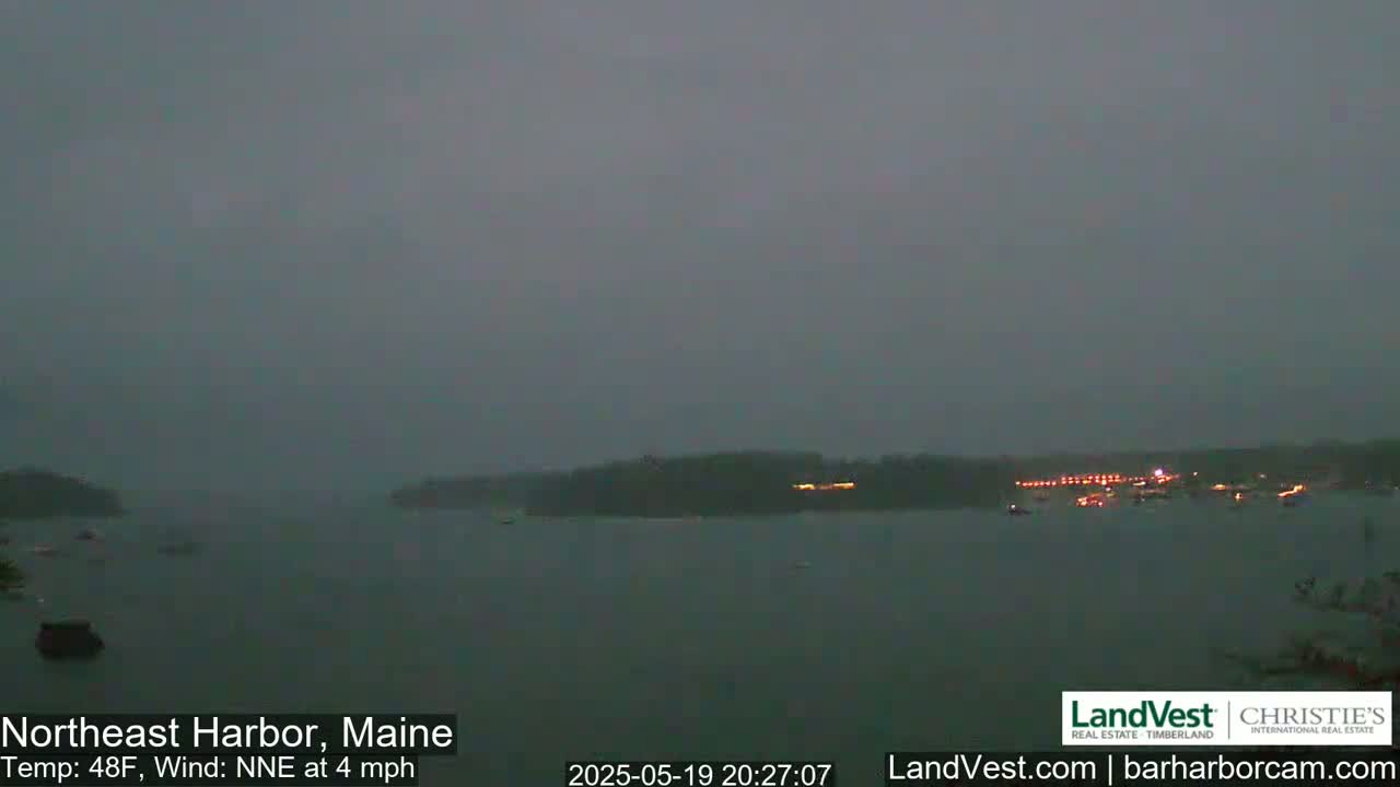 A dark, overcast view of a harbor at night with a few boats scattered across the water, under a 48°F temperature with a light northeast wind.