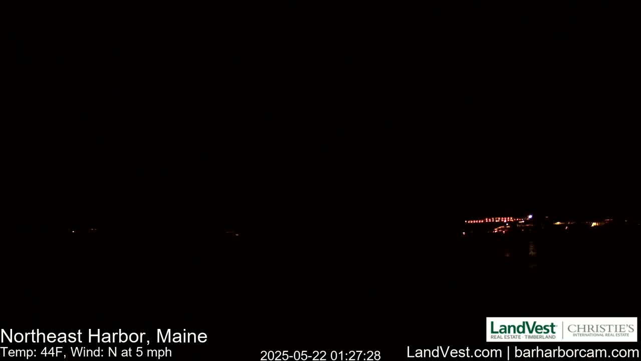 A nighttime, dark scene shows a distant line of lights across a body of water under a clear, dark sky with a north wind at 5 mph and a temperature of 44°F.