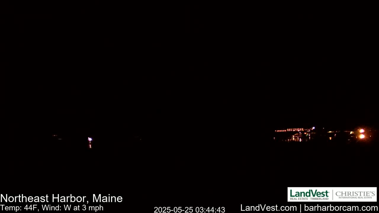 A dark nighttime scene shows a dimly lit shoreline across a body of water, with a 44°F temperature and a 3 mph west wind.
