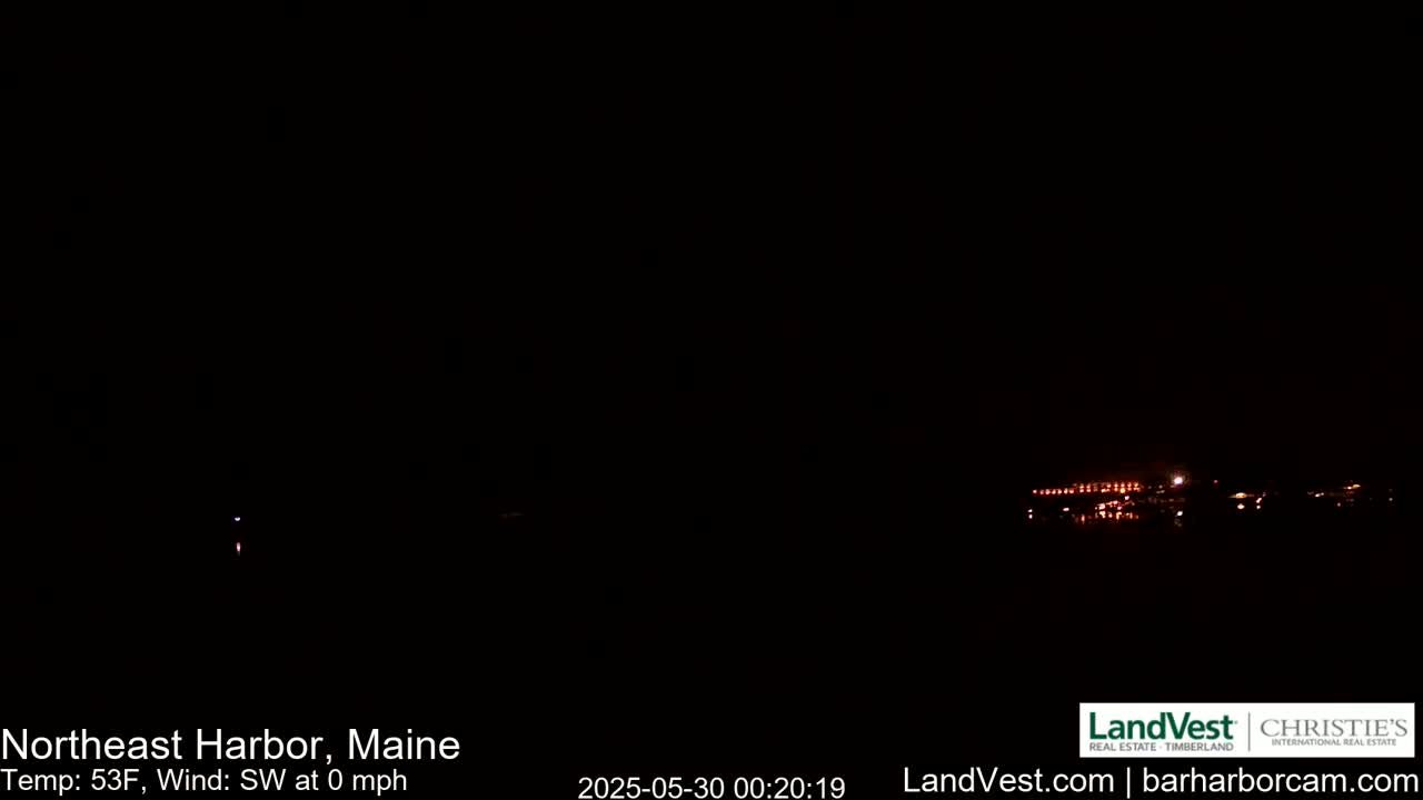 A nighttime view of faintly lit buildings in the distance under a dark sky with a calm southwest wind.