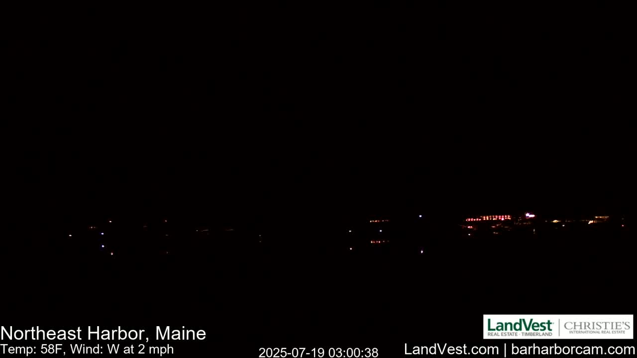 A nighttime, dark scene shows a distant line of lights across a dark body of water under a clear, dark sky, with a westerly wind at 2 mph and a temperature of 58°F.