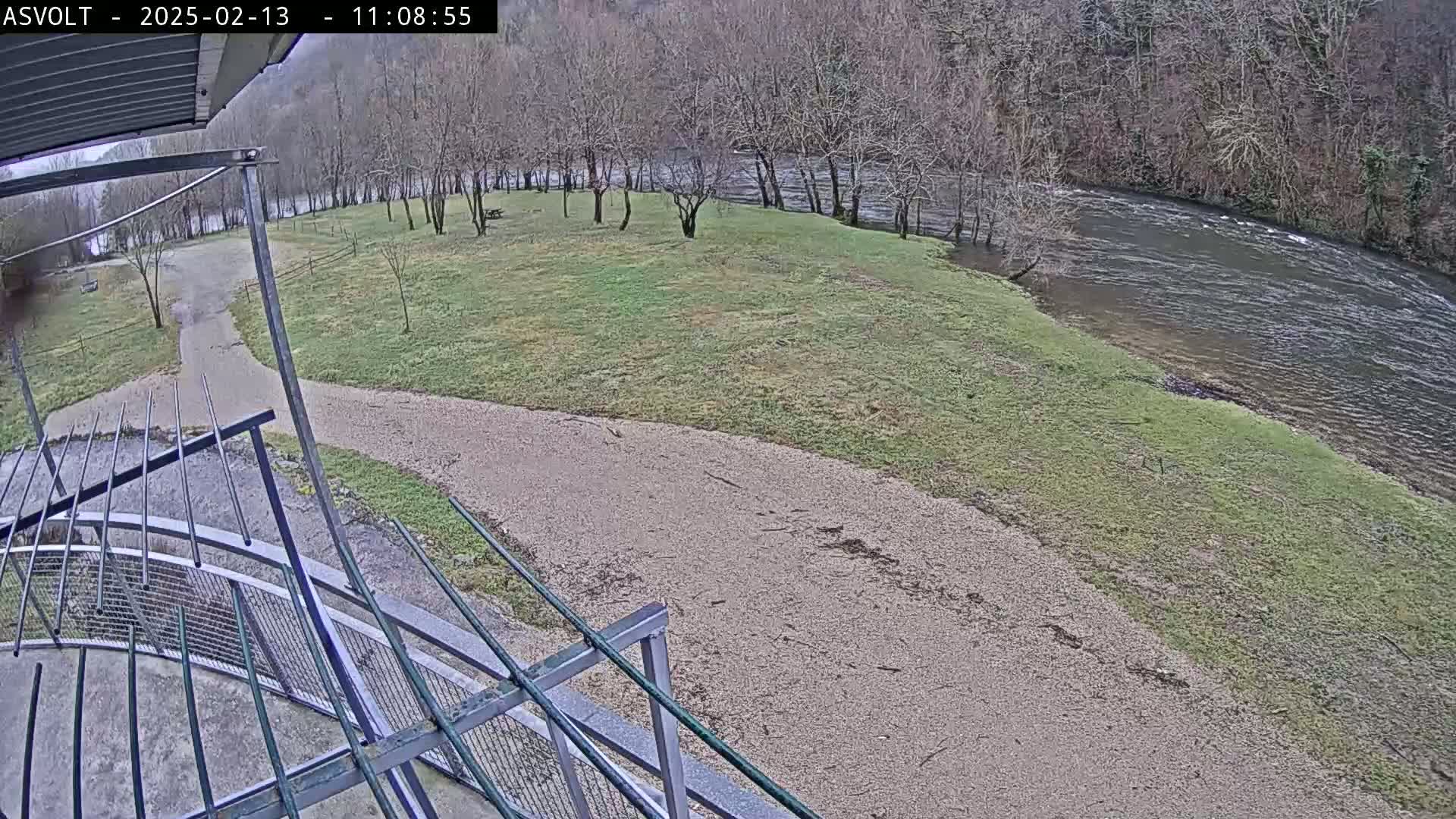 A gravel path leads to a grassy area beside a river under an overcast sky.