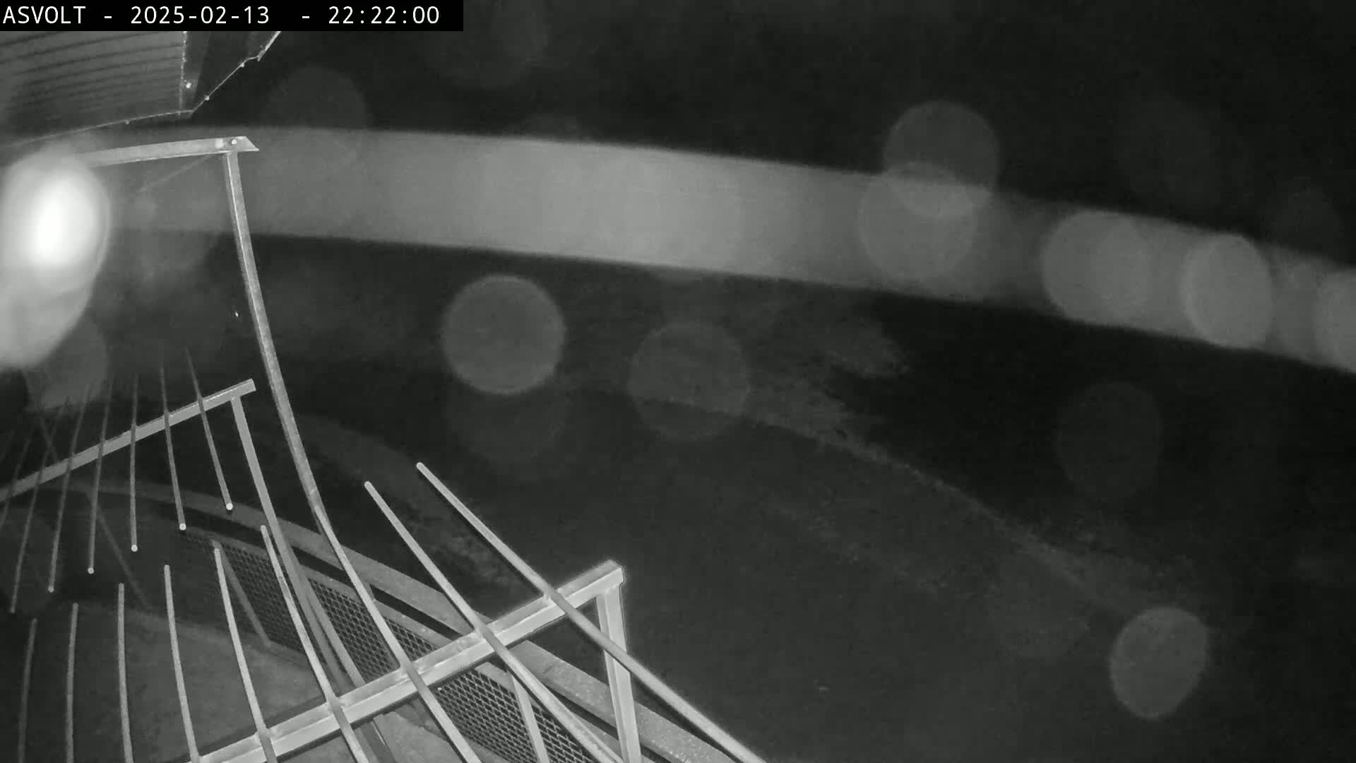 A nighttime, rainy view shows a metal railing and a blurred roadway beyond.