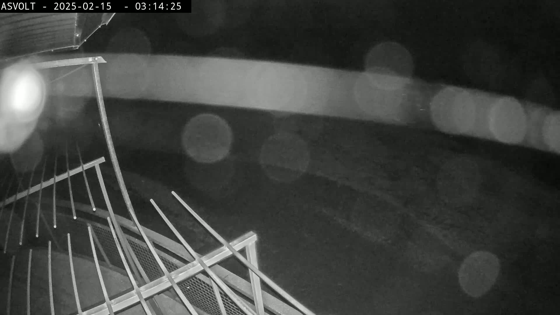 A nighttime, rainy view from above shows a metal railing and a dark, blurry ground below.