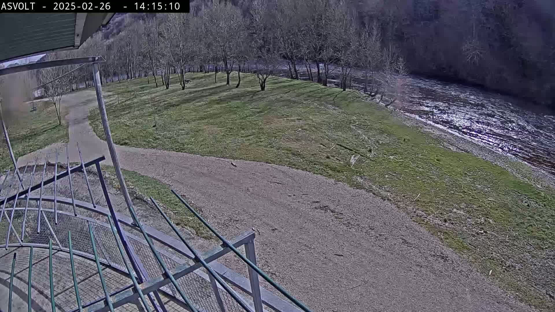 A gravel path leads to a grassy area next to a river under a partly sunny sky.