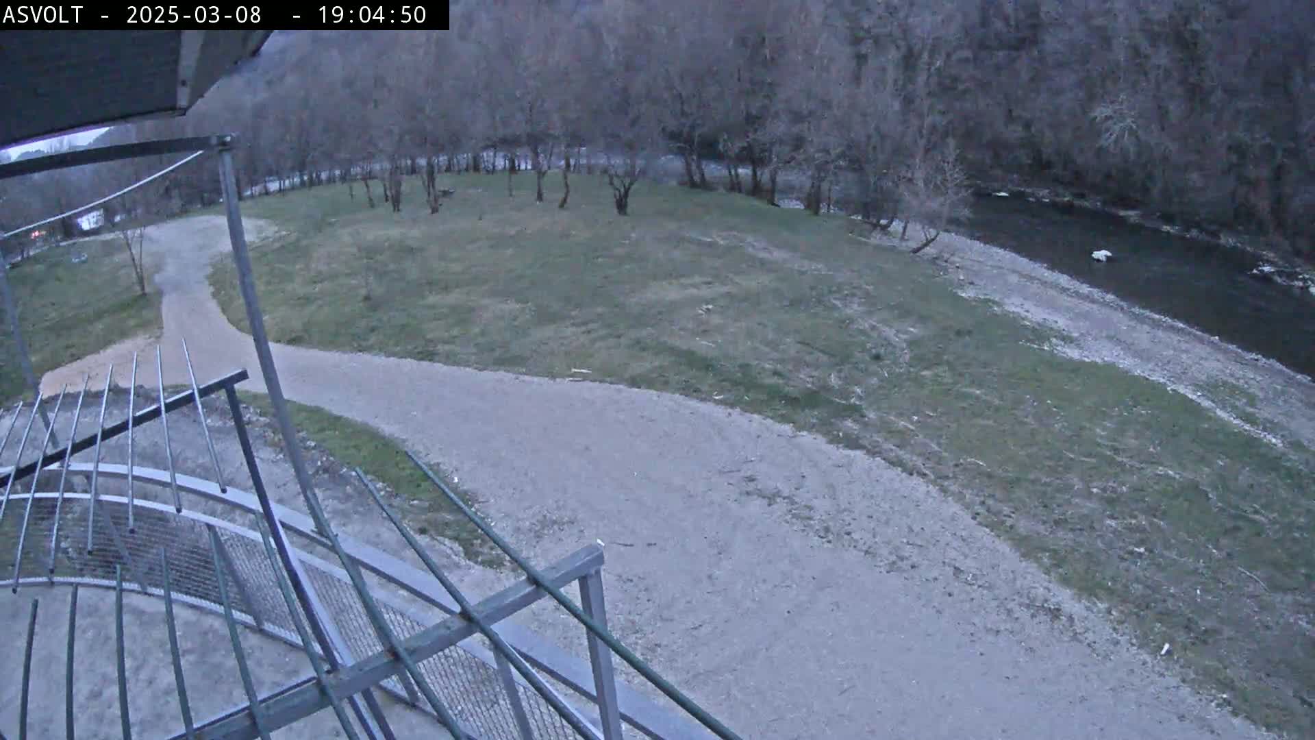 A gravel path curves around a grassy area next to a river under a dusky sky.