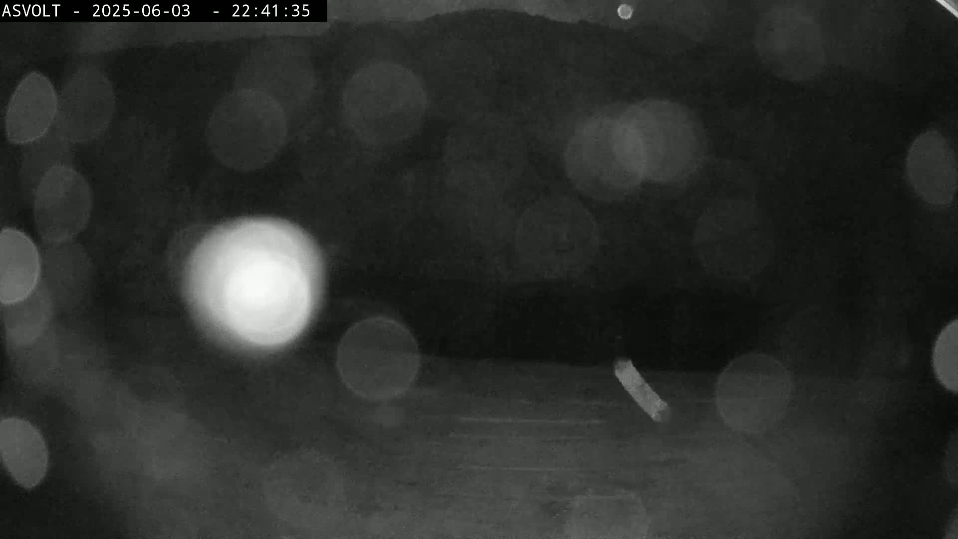 A grainy, blurry nighttime image shows out-of-focus lights and a dark ground with a faint line.