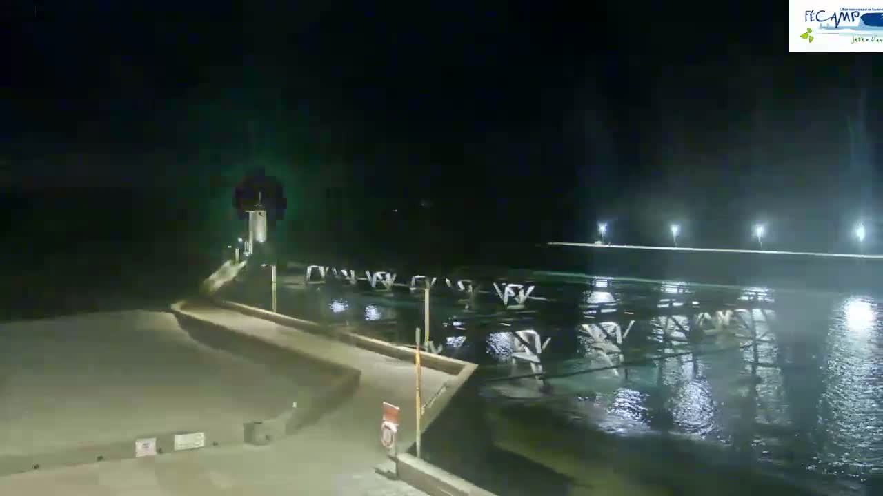 A nighttime view of a pier extending into dark, choppy water, illuminated by lights along the pier and embankment.