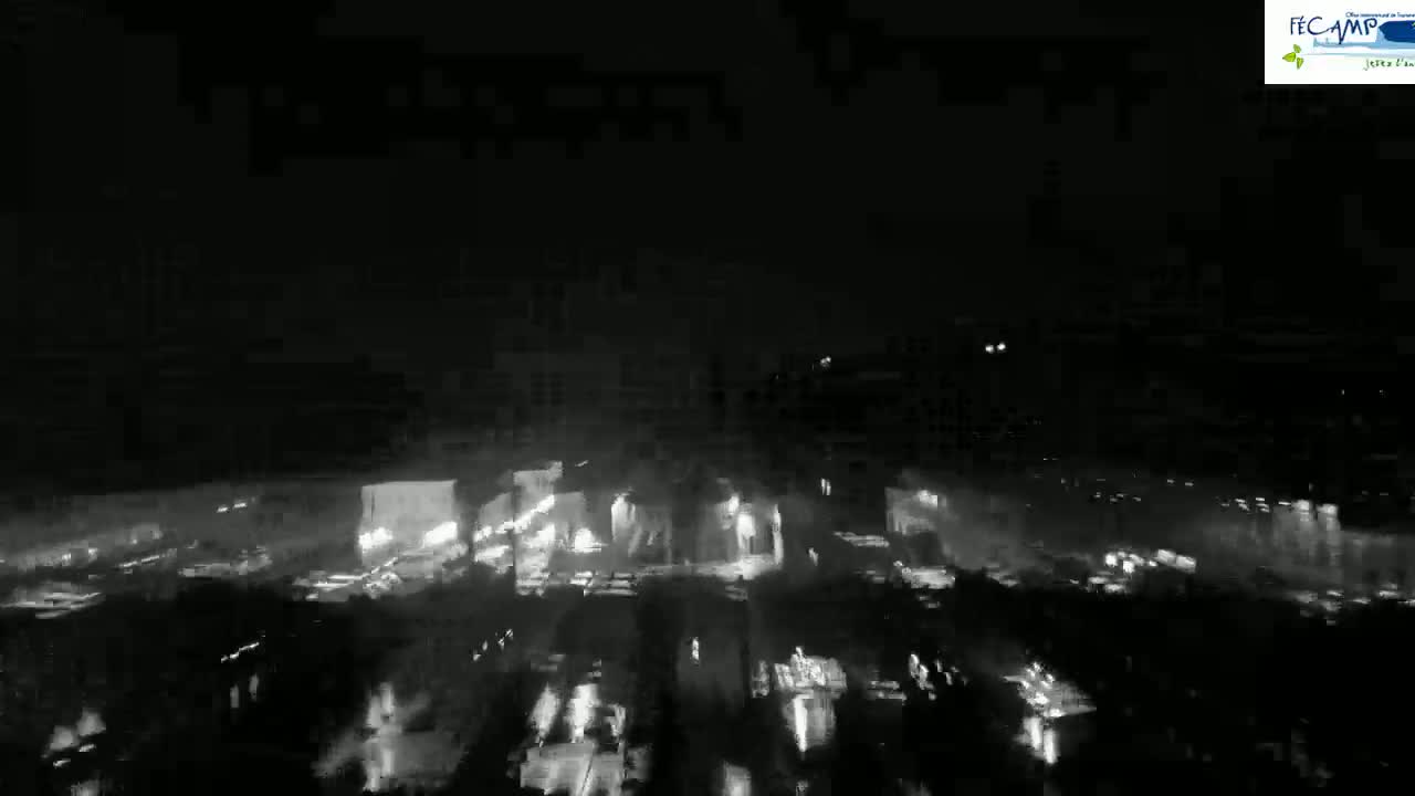 A nighttime, low-light view of a highway with many cars driving, appearing wet from rain or other precipitation.