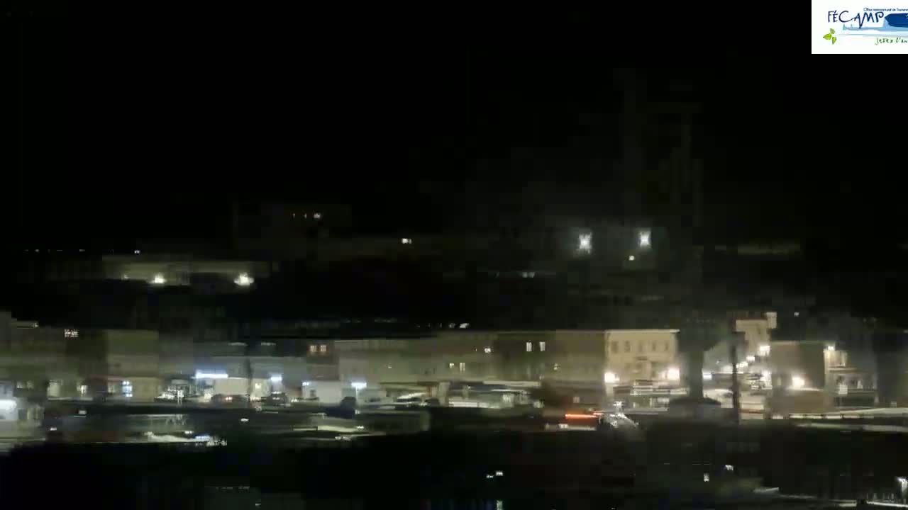 A nighttime long shot of a town or city with dimly lit buildings and a few vehicles visible on the streets.