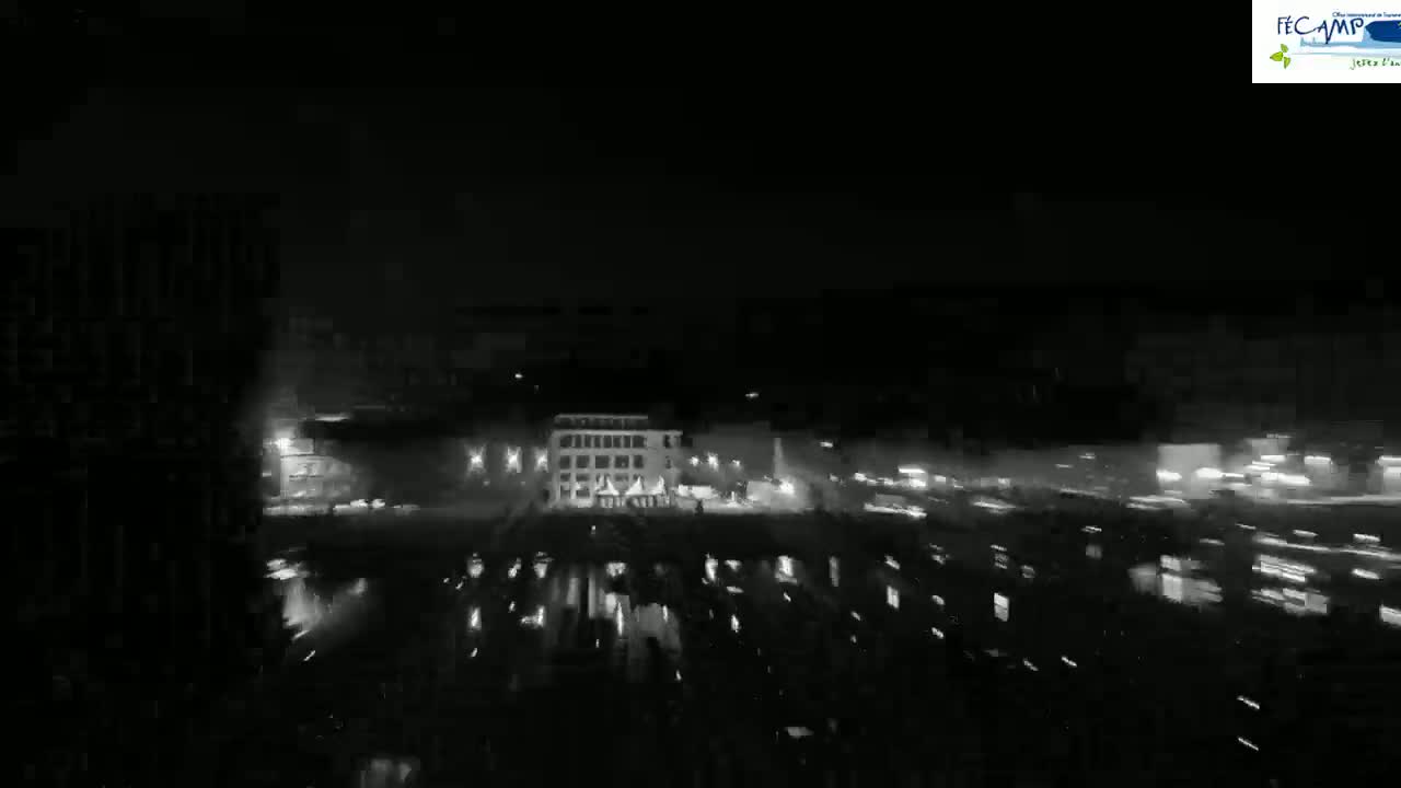 A nighttime, blurry view of a city square with buildings and streetlights visible, under dark, possibly rainy conditions.