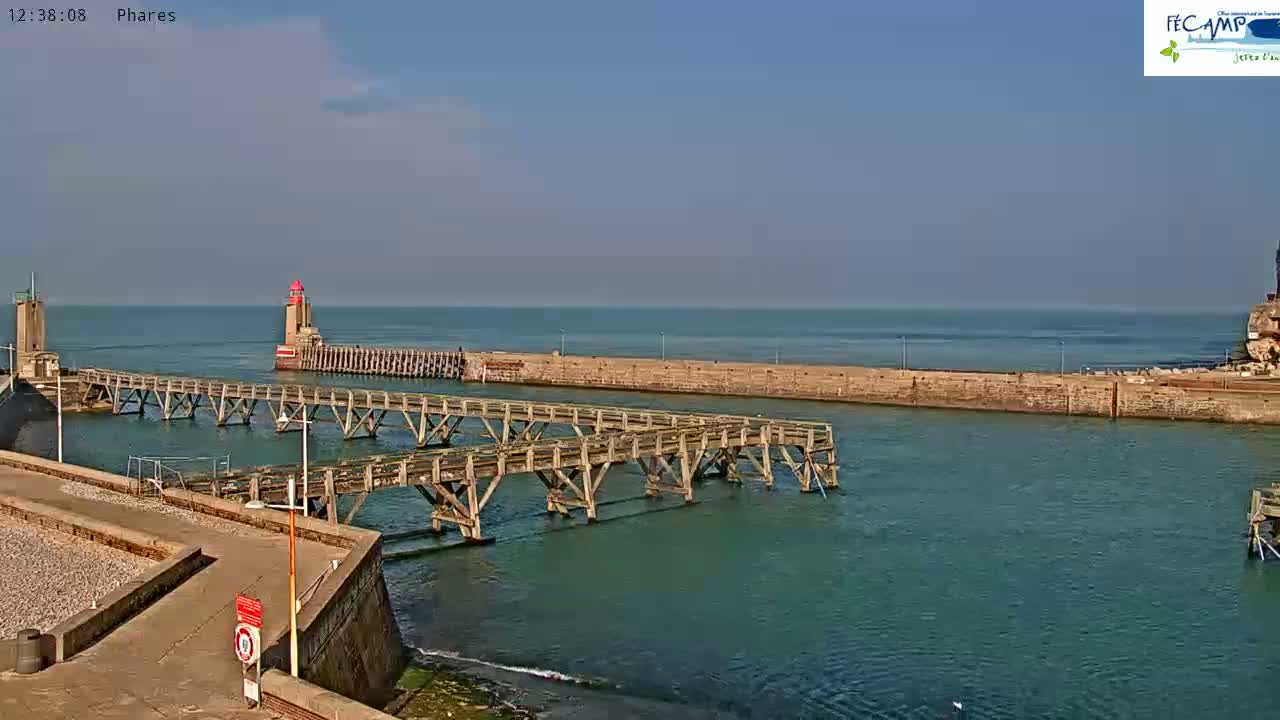 A harbor with two lighthouses, wooden walkways, and calm, blue-green water under a mostly sunny sky.
