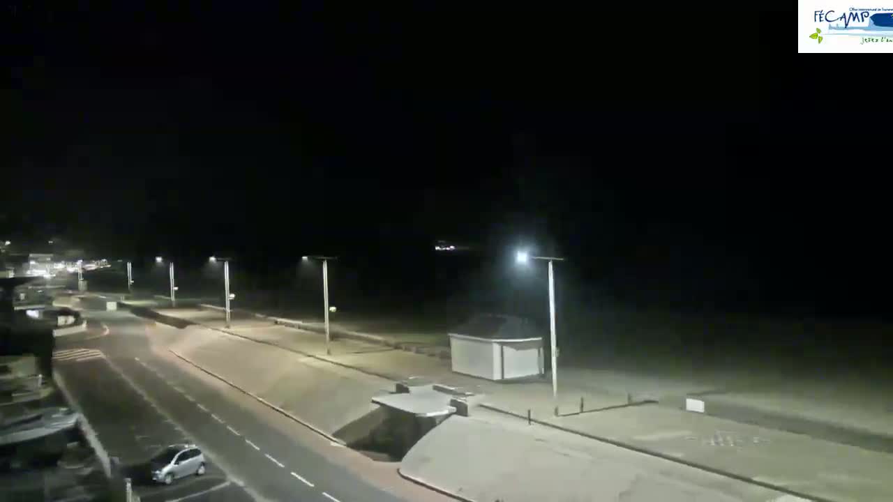 A nighttime view of a mostly empty seaside road with a beach in the background under a dark, cloudy sky.