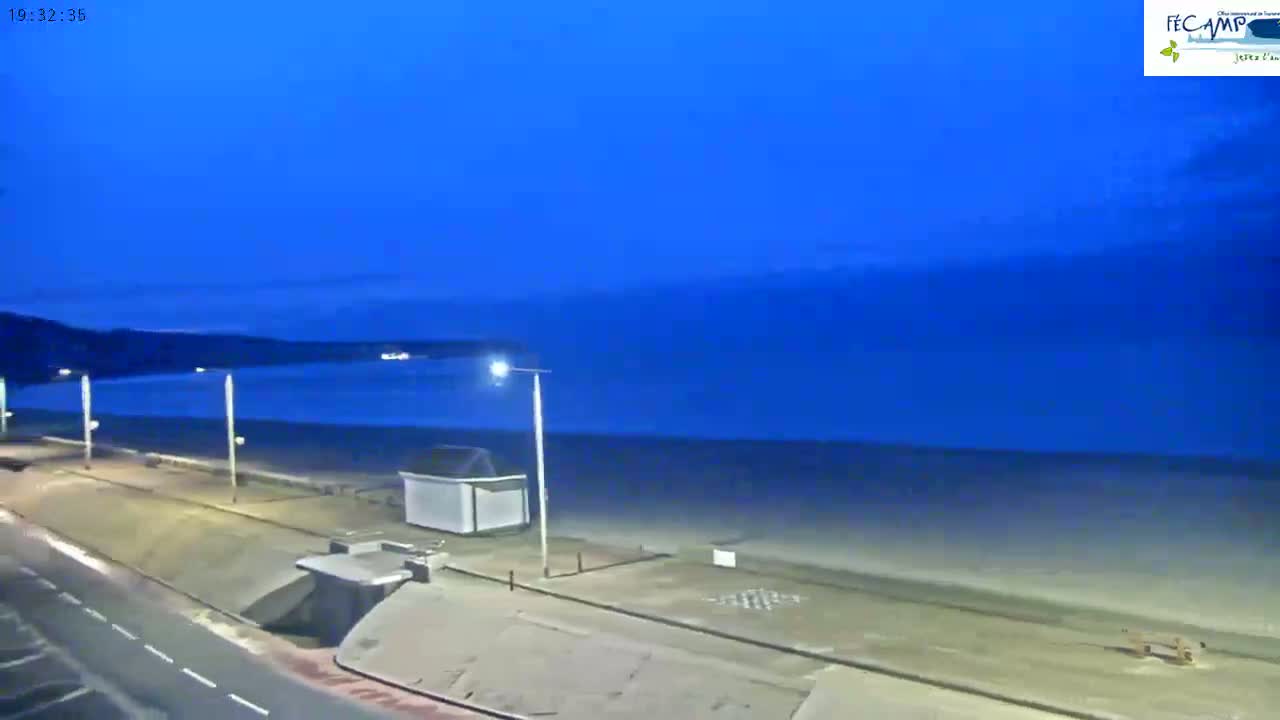 A dark-blue, twilight sky overlooks a mostly empty beach and a paved walkway next to a road.