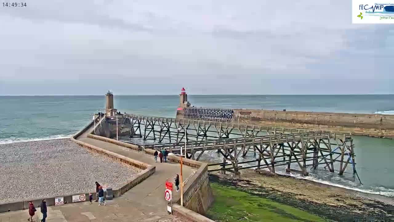 A long wooden pier extends from a rocky beach toward two lighthouses, under a mostly cloudy sky with a slightly choppy sea.