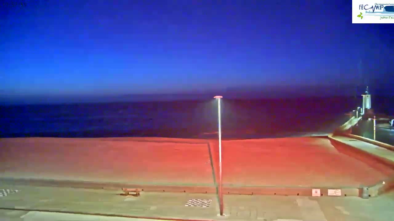 A dark-blue, twilight sky overlooks a red-lit beach, calm ocean, and a tall lamppost.