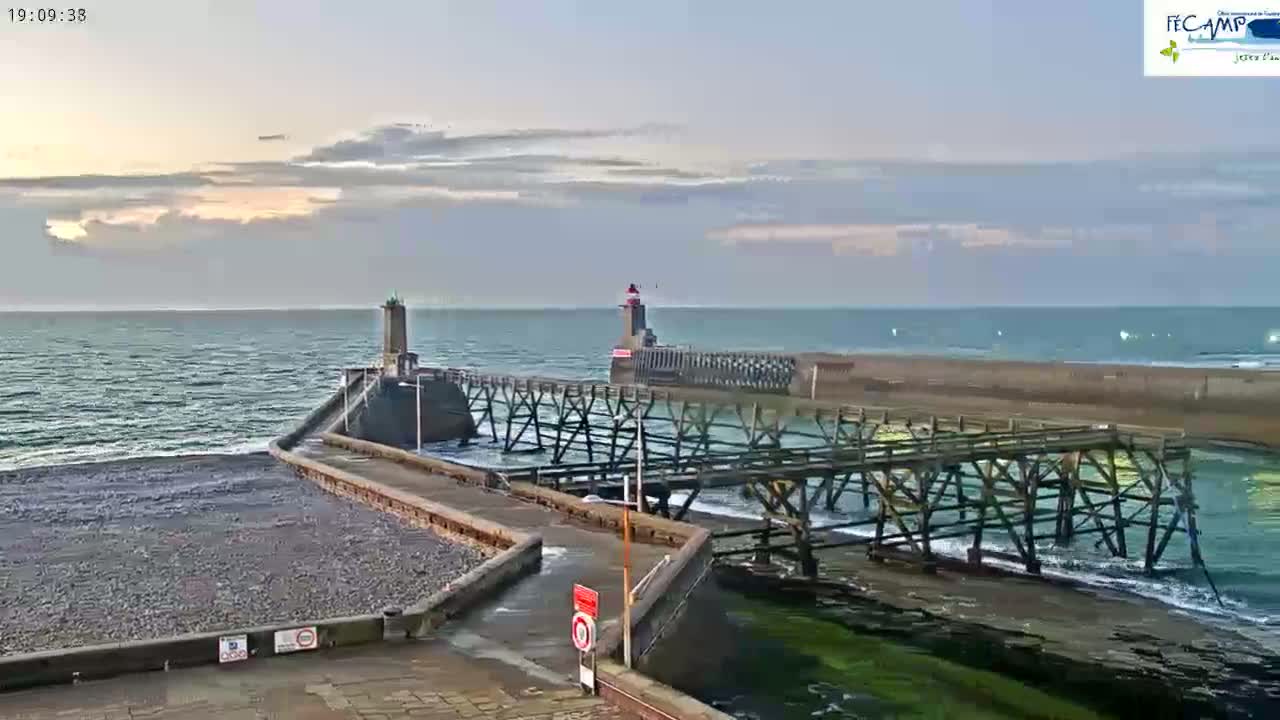 A long pier with two lighthouses extends into a calm, overcast ocean.