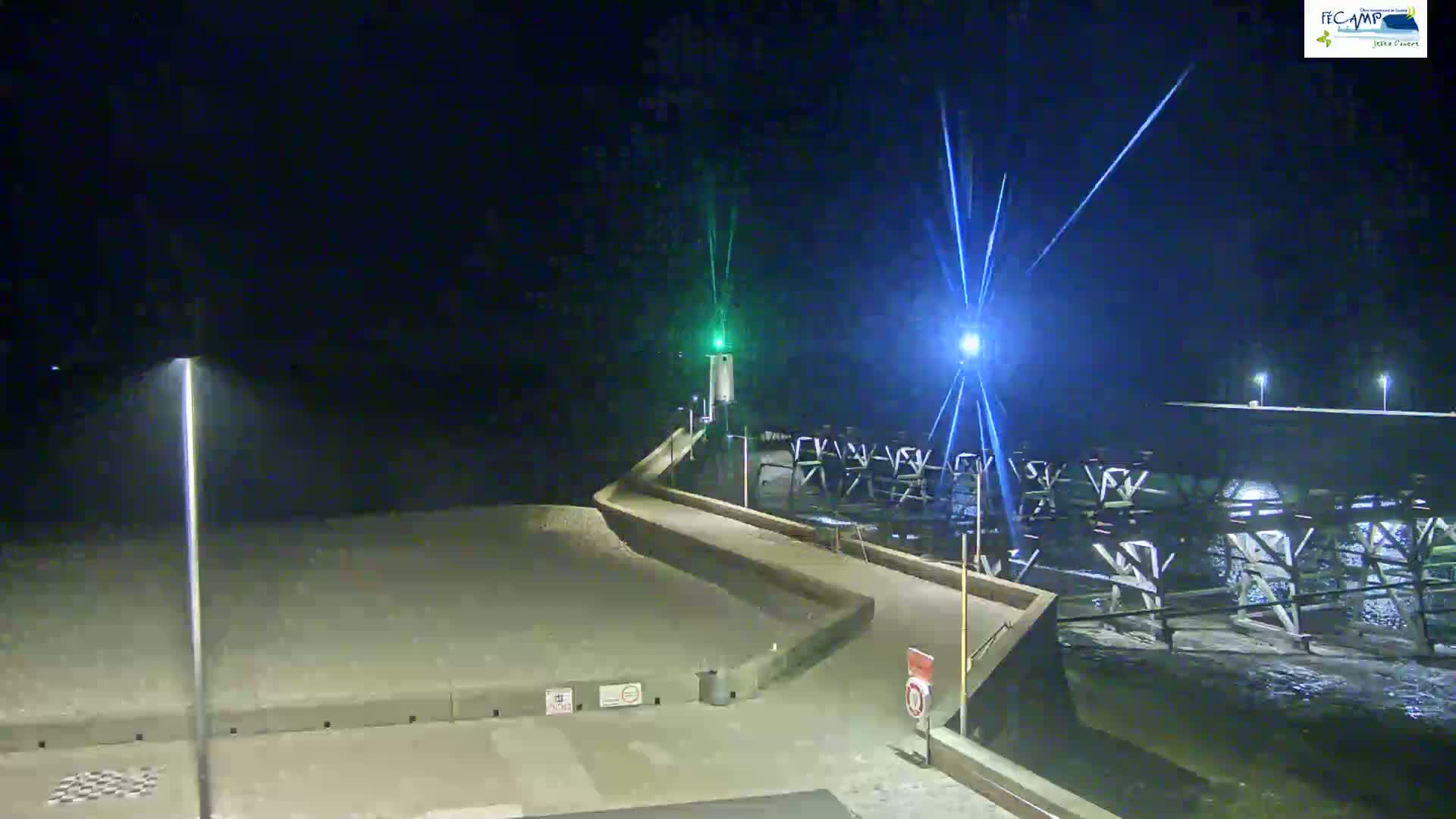A nighttime view of a pier extending into dark water under bright lights, with a small lighthouse visible at the pier's end.