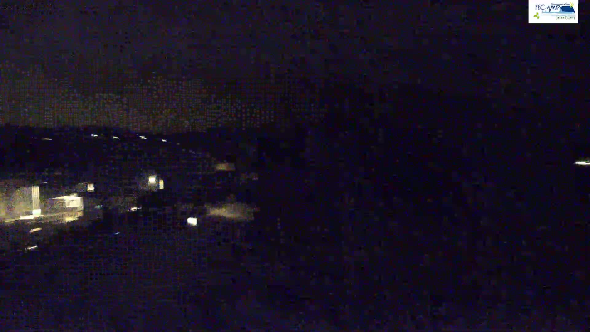 A nighttime, dark aerial view shows a dimly lit area with buildings and a few scattered lights.