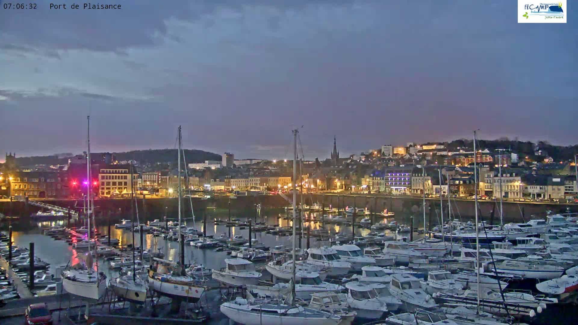 A harbor filled with many boats is situated in front of a town at twilight under a mostly clear sky.