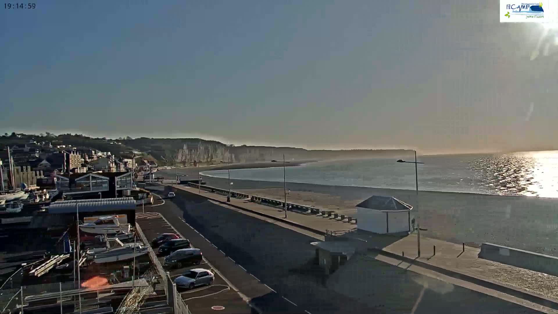 A coastal town with a beach and white cliffs is visible under a clear, bright sky, with calm water reflecting sunlight.