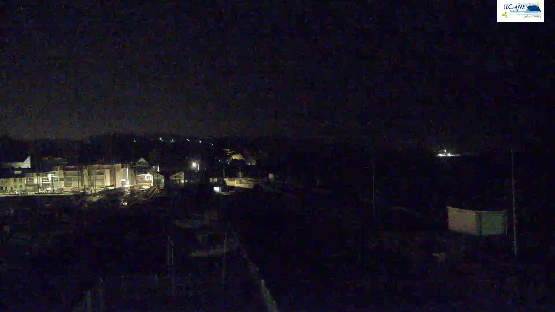 A nighttime, low-light view of a harbor with buildings and boats, under a dark sky.