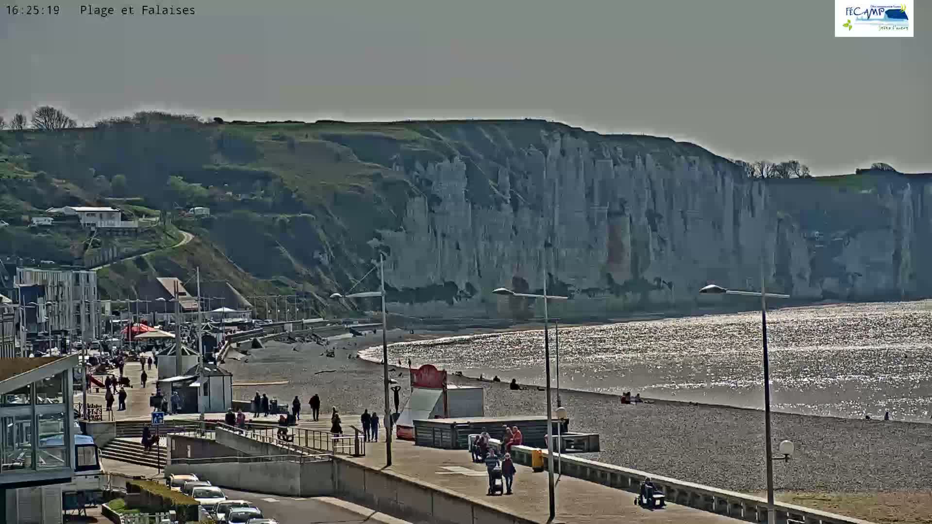 A sunny day at a beach with a pebble shore and tall white cliffs in the background.